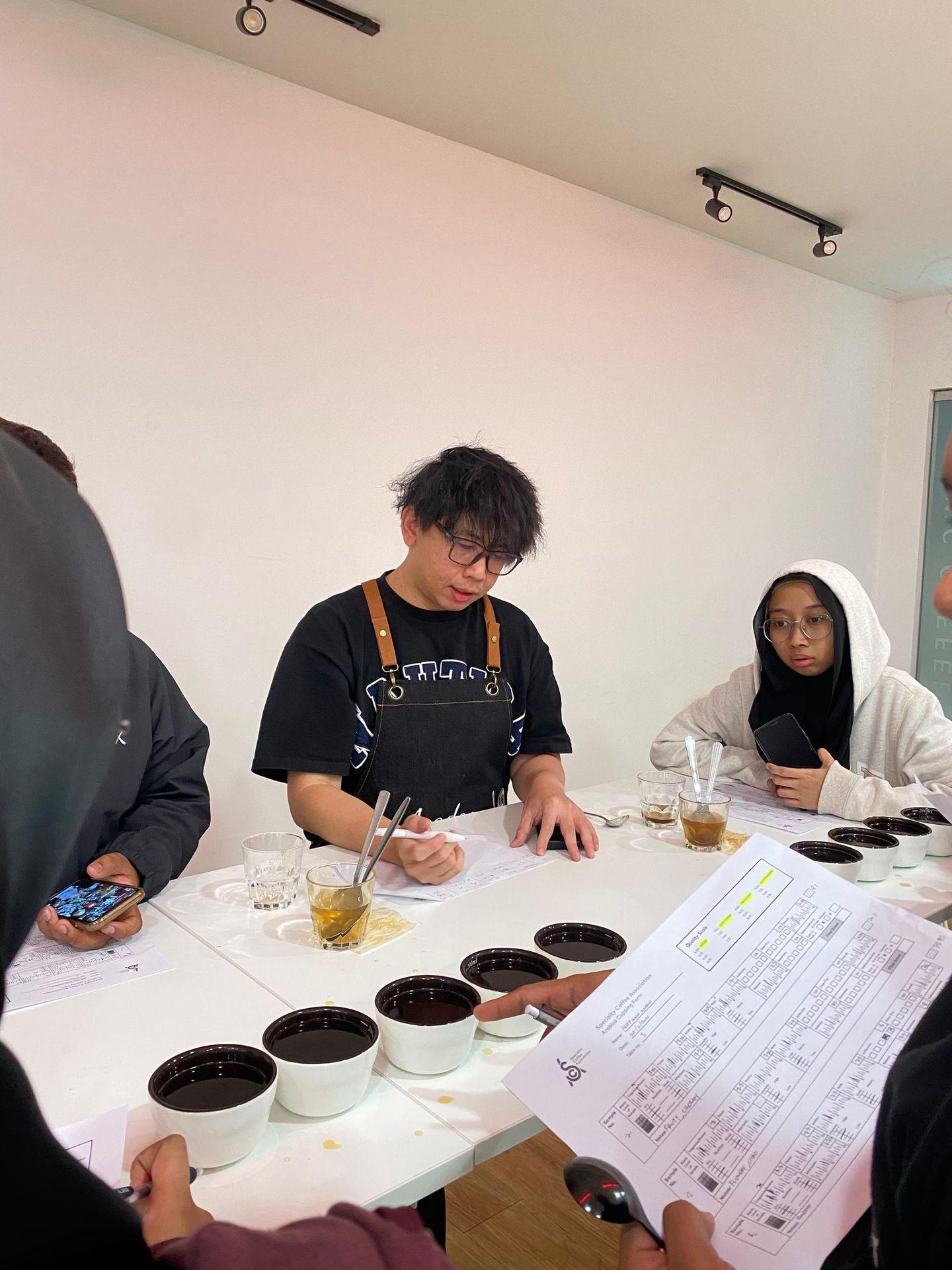 CAN Academy AST trainer leading coffee cupping with SCA score sheets and spoons in Kuala Lumpur